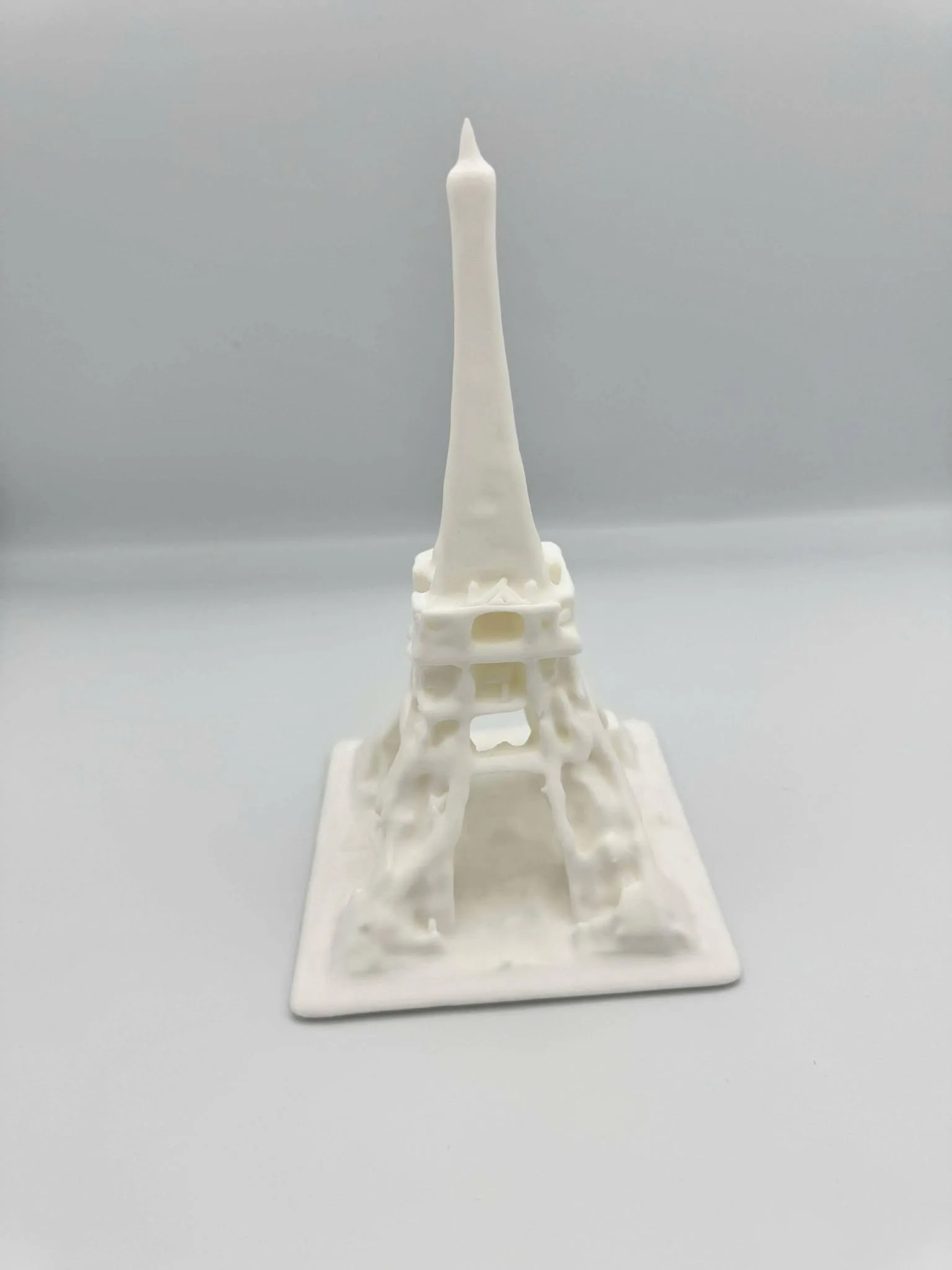 En hvid 3D-printet model af Eiffeltårnet på en firkantet sokkel, cirka 20 centimeter høj, med gitterstrukturen i tårnet gengivet som ophøjede ribber.